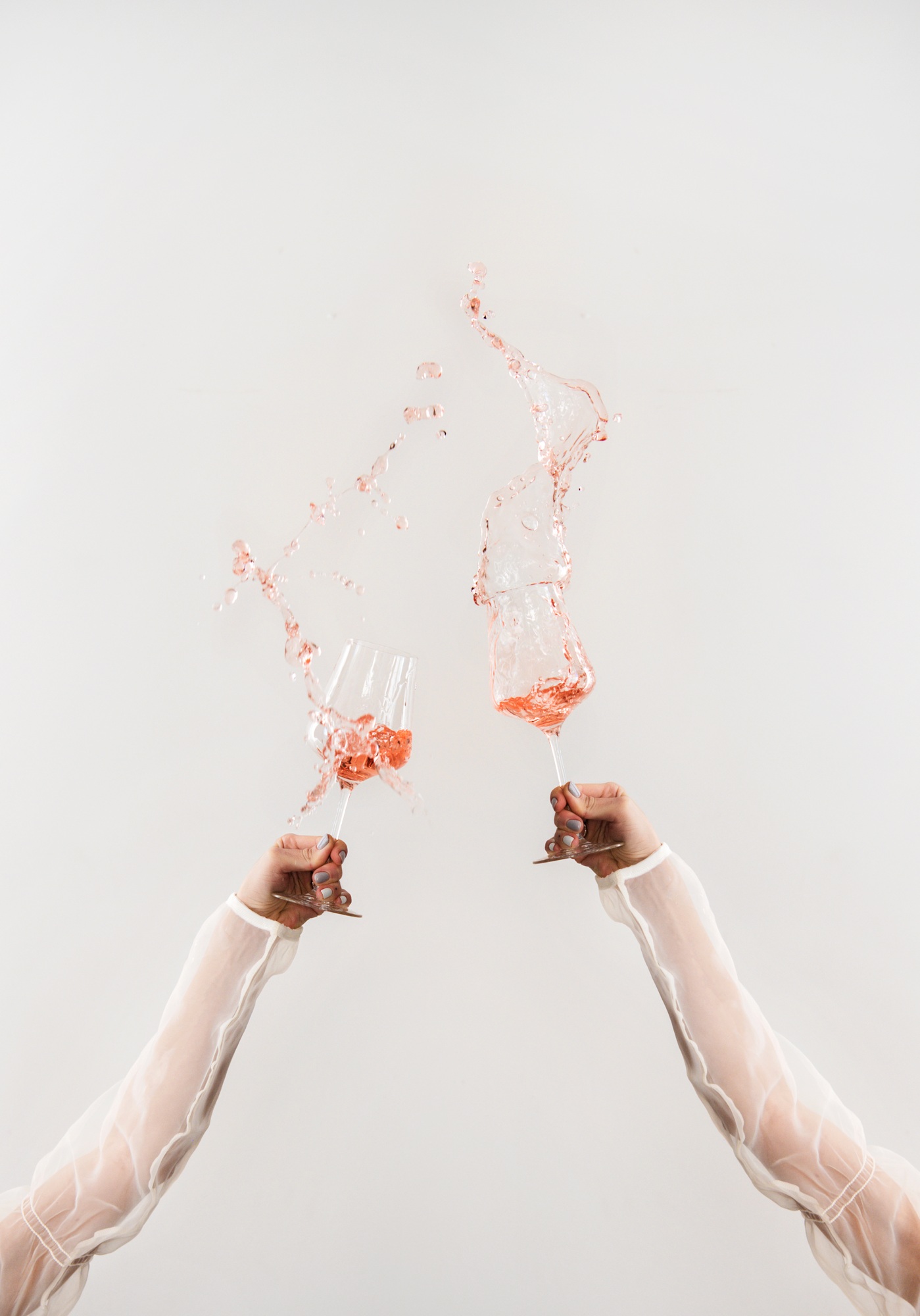 Female hands clinking glasses of rose wine making splashes